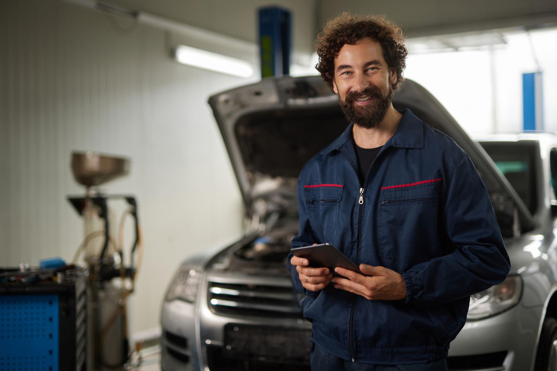 Car mechanic smiling and holding tablet in auto repair shop