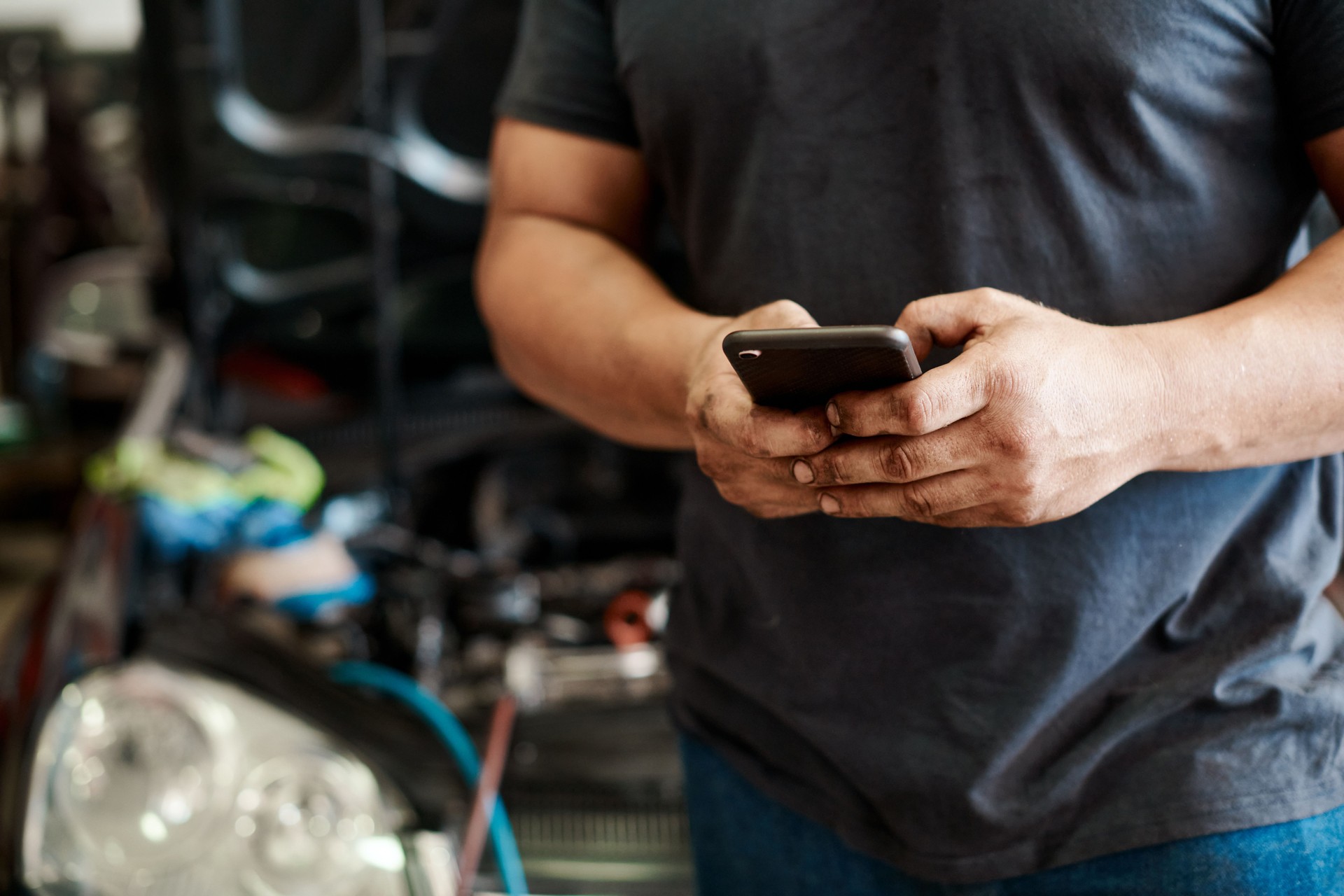 Shot of a mechanic using his cellphone while working in an auto repair shop